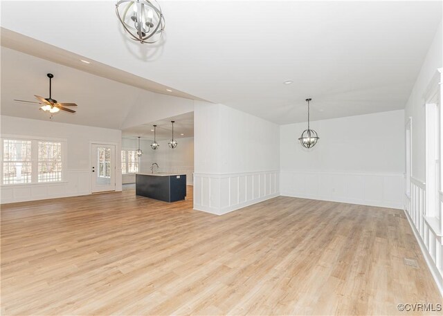 unfurnished living room with vaulted ceiling, sink, ceiling fan with notable chandelier, and light wood-type flooring