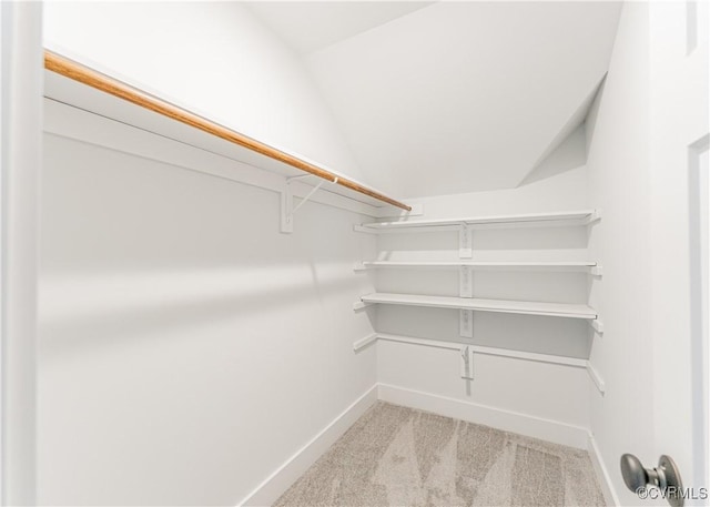 walk in closet with vaulted ceiling and light colored carpet