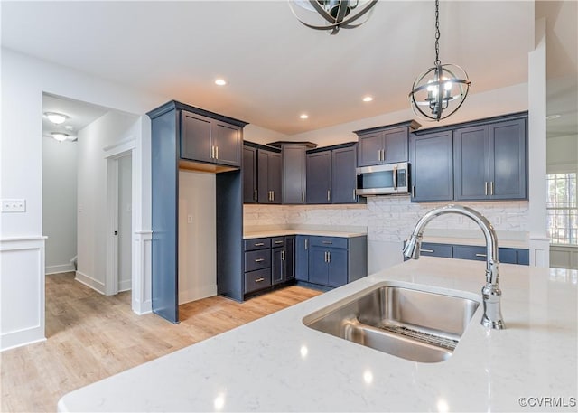 kitchen with sink, backsplash, light stone counters, and decorative light fixtures