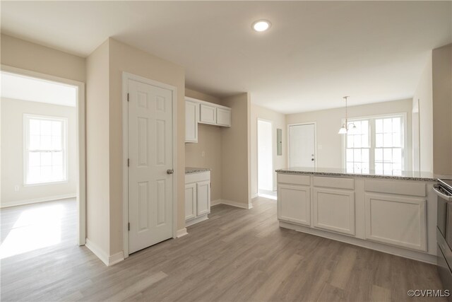 kitchen featuring white cabinets, hanging light fixtures, stainless steel stove, light hardwood / wood-style floors, and light stone counters