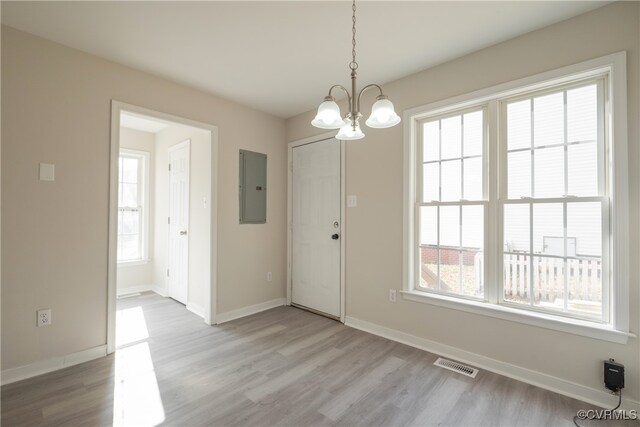 unfurnished dining area with a notable chandelier, electric panel, light wood-type flooring, and a wealth of natural light