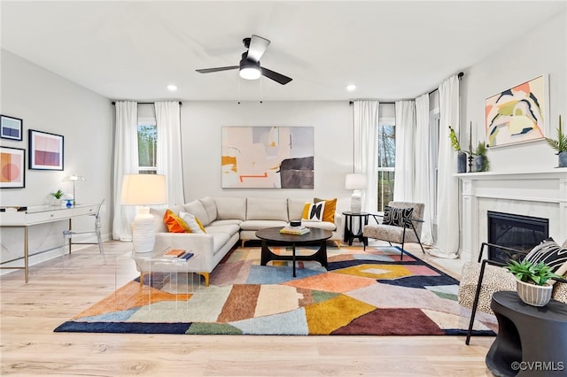 living room with ceiling fan, a high end fireplace, and light hardwood / wood-style flooring