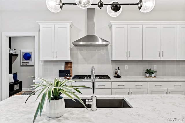 kitchen featuring wall chimney range hood, white cabinets, light stone counters, and decorative backsplash