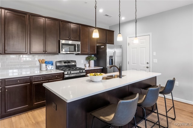 kitchen featuring appliances with stainless steel finishes, light hardwood / wood-style floors, hanging light fixtures, and an island with sink