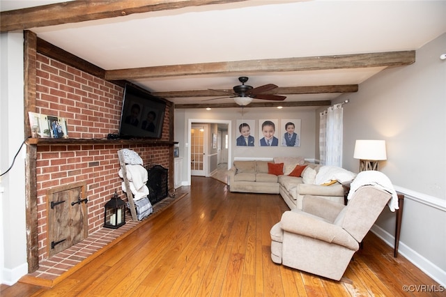 living room with hardwood / wood-style floors, ceiling fan, beam ceiling, and a fireplace