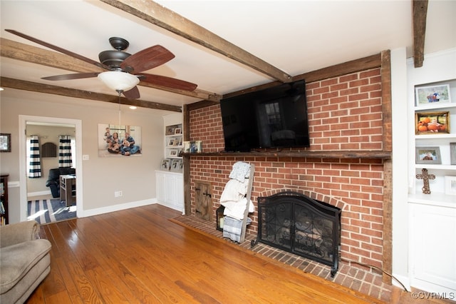 living room with beam ceiling, ceiling fan, wood-type flooring, and a brick fireplace