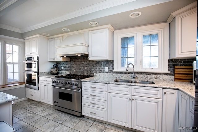 kitchen with backsplash, premium range hood, stainless steel appliances, sink, and white cabinetry