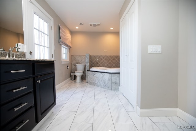 bathroom with vanity, tiled bath, and toilet