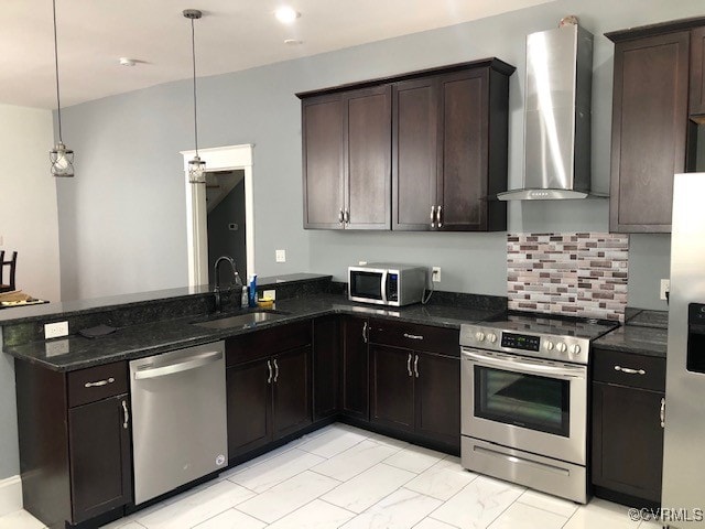 kitchen with appliances with stainless steel finishes, dark brown cabinets, sink, wall chimney range hood, and hanging light fixtures