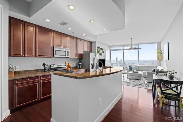 kitchen featuring visible vents, appliances with stainless steel finishes, expansive windows, dark wood finished floors, and a center island with sink