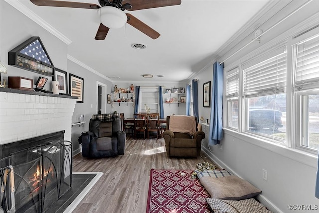 living room with ceiling fan, crown molding, wood-type flooring, and a fireplace