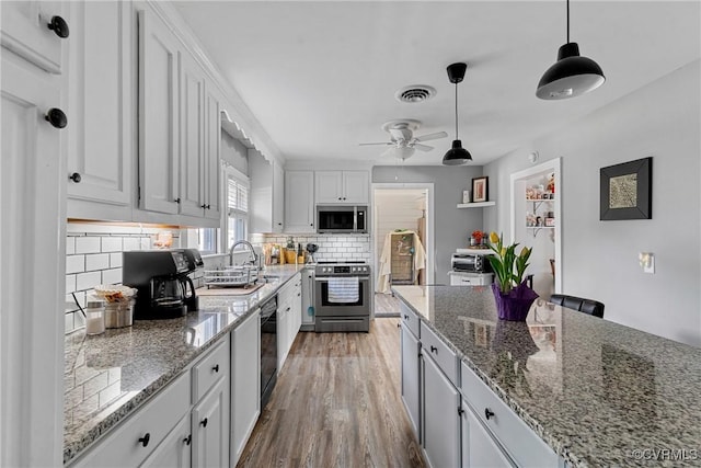 kitchen with backsplash, light wood-type flooring, appliances with stainless steel finishes, decorative light fixtures, and white cabinetry