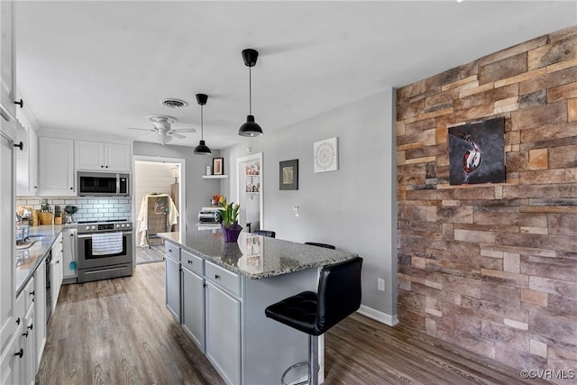 kitchen with stone counters, white cabinetry, a center island, stainless steel appliances, and decorative backsplash