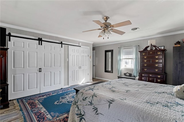 bedroom featuring a barn door, ceiling fan, crown molding, and wood-type flooring