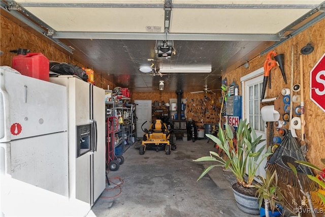 garage featuring white refrigerator with ice dispenser, a workshop area, a garage door opener, and wooden walls