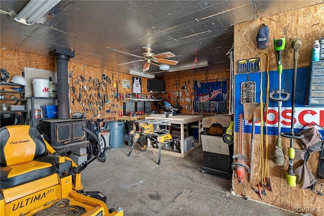 misc room with a workshop area, ceiling fan, a wood stove, and concrete flooring