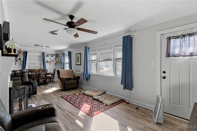 living room featuring hardwood / wood-style flooring, ceiling fan, a fireplace, and crown molding