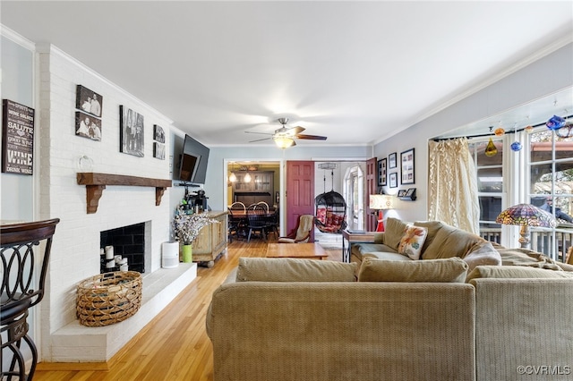 living room with a fireplace, ceiling fan, crown molding, and wood-type flooring