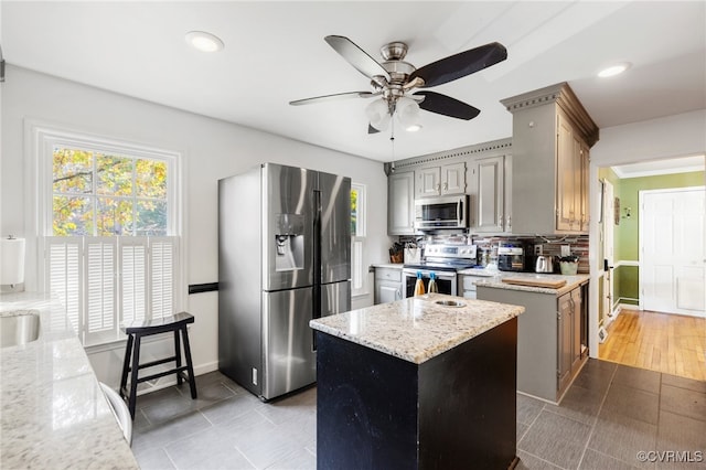 kitchen featuring backsplash, light stone counters, gray cabinetry, stainless steel appliances, and a kitchen island