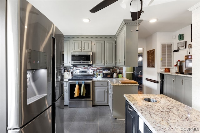 kitchen featuring ceiling fan, gray cabinets, a kitchen island, light stone counters, and stainless steel appliances