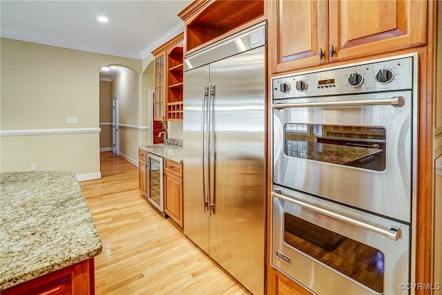 kitchen with light hardwood / wood-style floors, light stone countertops, stainless steel appliances, and beverage cooler