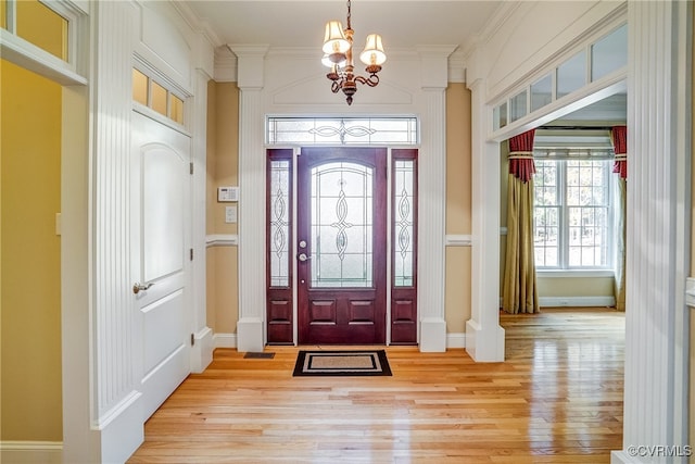 foyer entrance with light wood-type flooring, ornamental molding, and an inviting chandelier