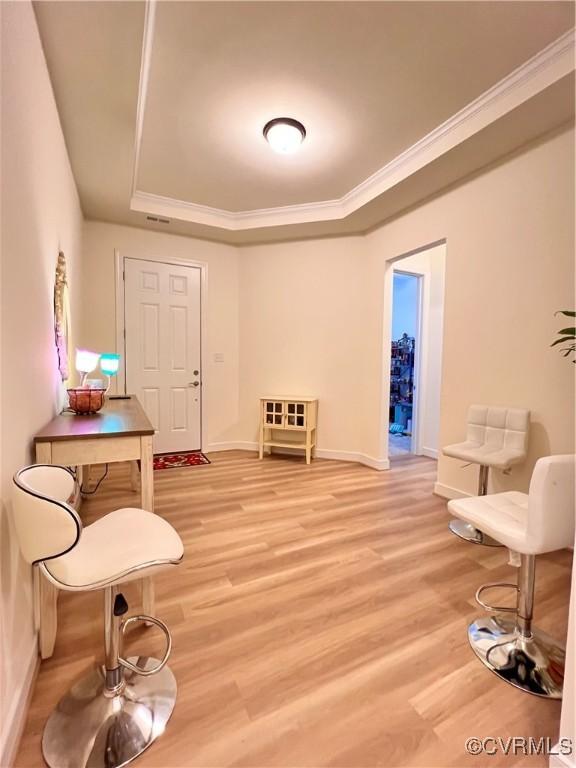 living area with a raised ceiling, crown molding, and light hardwood / wood-style flooring