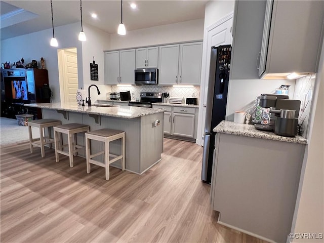 kitchen with pendant lighting, sink, a kitchen island with sink, light stone counters, and stainless steel appliances