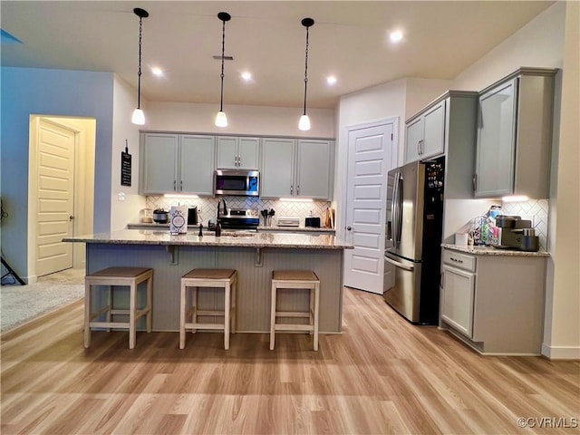 kitchen featuring gray cabinets, hanging light fixtures, stainless steel appliances, light stone countertops, and an island with sink