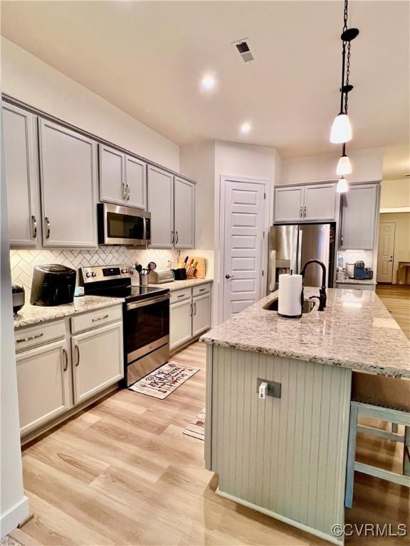 kitchen featuring hanging light fixtures, appliances with stainless steel finishes, a kitchen island with sink, and decorative backsplash