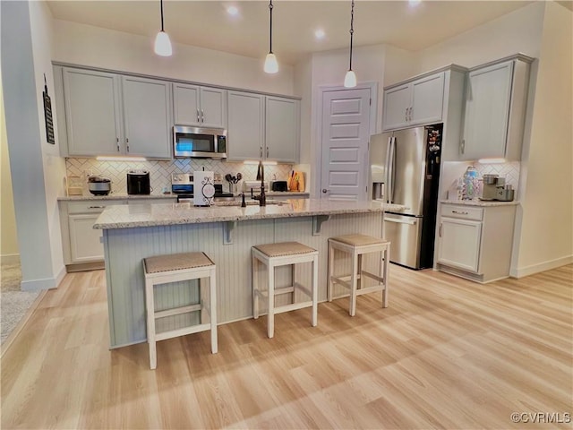 kitchen with light hardwood / wood-style flooring, gray cabinets, a kitchen island with sink, stainless steel appliances, and light stone counters