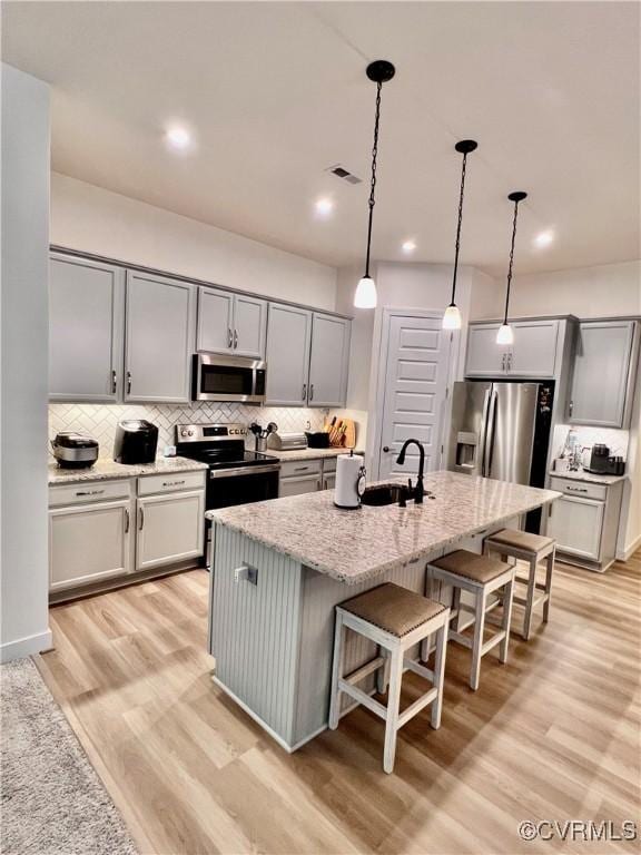 kitchen featuring appliances with stainless steel finishes, sink, hanging light fixtures, light stone countertops, and a center island with sink