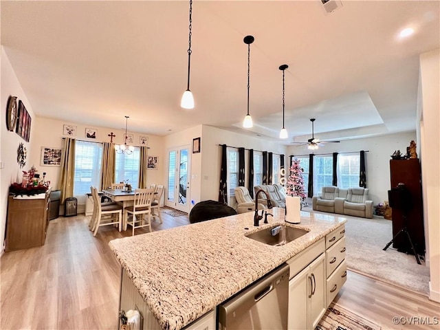 kitchen with pendant lighting, sink, dishwasher, light stone counters, and a center island with sink