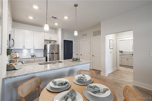 kitchen featuring light stone countertops, white cabinetry, sink, stainless steel appliances, and decorative light fixtures