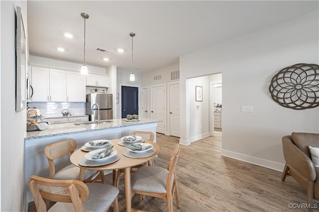 kitchen with sink, hanging light fixtures, light hardwood / wood-style flooring, stainless steel fridge, and white cabinetry