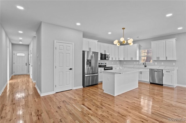 kitchen with appliances with stainless steel finishes, white cabinets, a center island, and pendant lighting