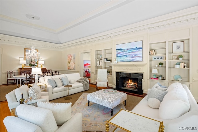 living room with built in shelves, a high end fireplace, a notable chandelier, hardwood / wood-style floors, and ornamental molding