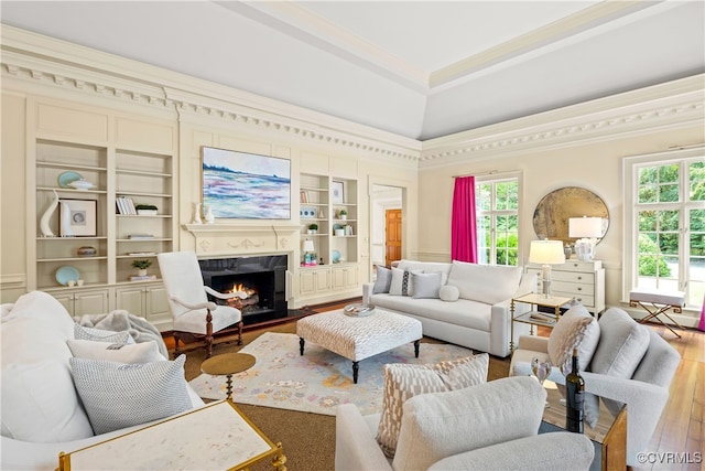 living room featuring a towering ceiling, crown molding, wood-type flooring, built in features, and a premium fireplace