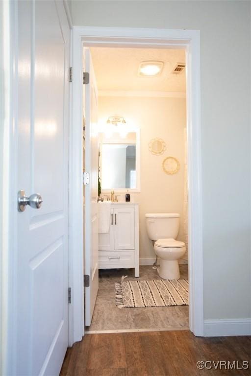 bathroom featuring ornamental molding, vanity, wood-type flooring, and toilet