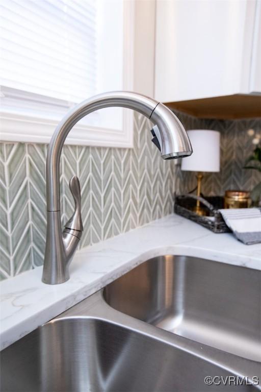 room details featuring white cabinets, light stone countertops, sink, and tasteful backsplash