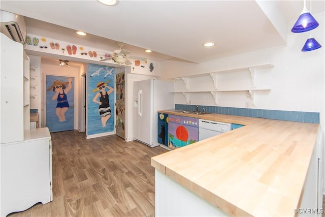 kitchen featuring white appliances, butcher block counters, white cabinetry, hanging light fixtures, and a wall mounted air conditioner