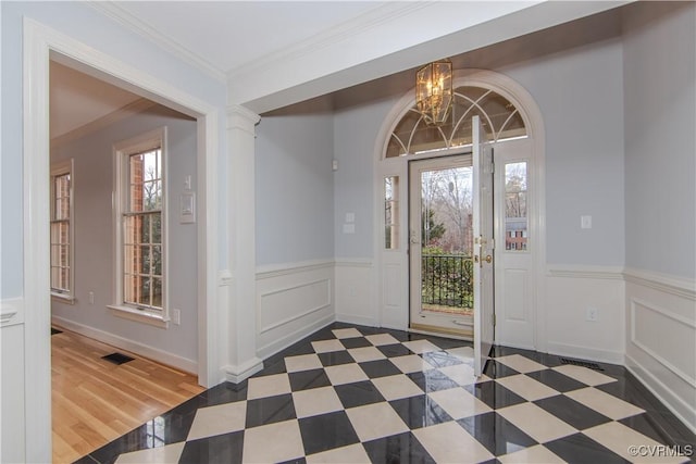 foyer entrance featuring ornamental molding, wainscoting, visible vents, and an inviting chandelier