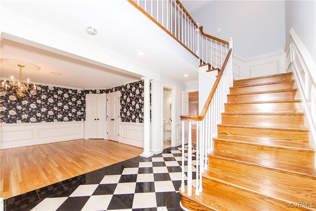 entryway featuring stairway, an inviting chandelier, crown molding, ornate columns, and a decorative wall