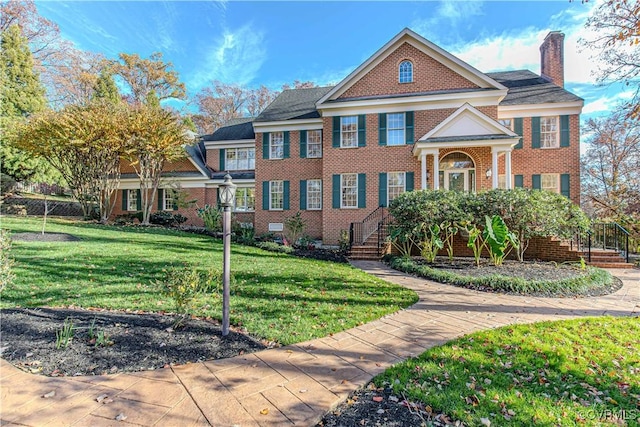 view of front of property featuring brick siding, a chimney, and a front yard