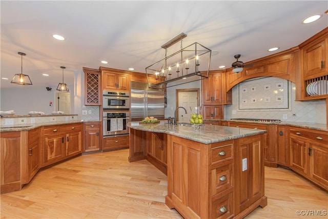 kitchen with stainless steel appliances, brown cabinetry, a kitchen island with sink, and decorative light fixtures