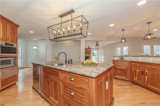 kitchen featuring a center island with sink, brown cabinets, decorative light fixtures, stainless steel appliances, and a sink