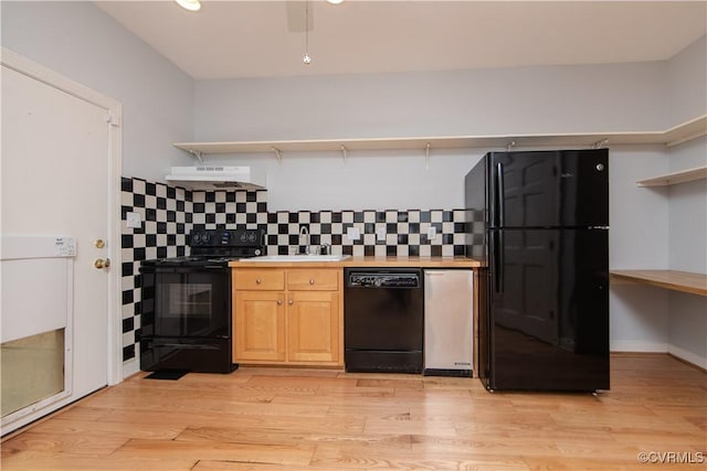 kitchen featuring light wood-style flooring, under cabinet range hood, light countertops, black appliances, and tasteful backsplash