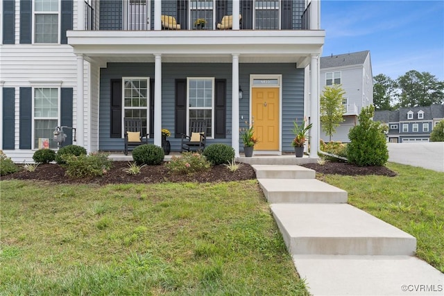 property entrance featuring a lawn, a balcony, and covered porch