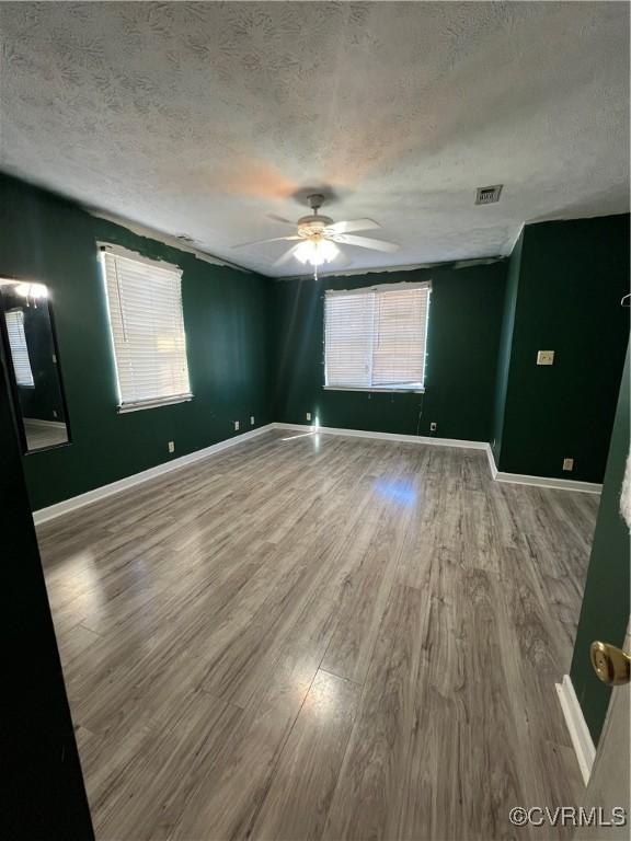 spare room featuring a textured ceiling, hardwood / wood-style flooring, a wealth of natural light, and ceiling fan