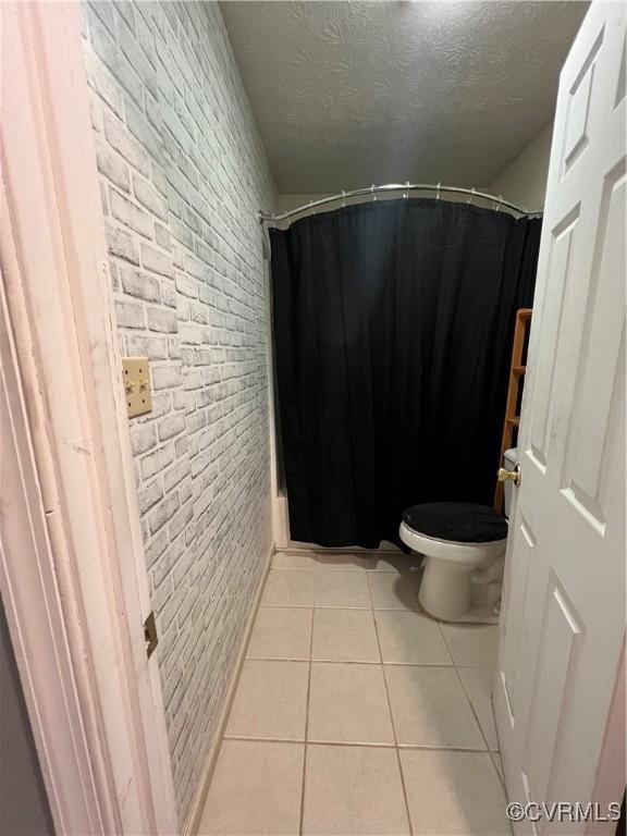 bathroom with walk in shower, tile patterned flooring, brick wall, a textured ceiling, and toilet